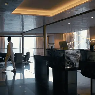 Modern luxury lobby with marble reception desks, ambient lighting, and a person walking past floor-to-ceiling windows.