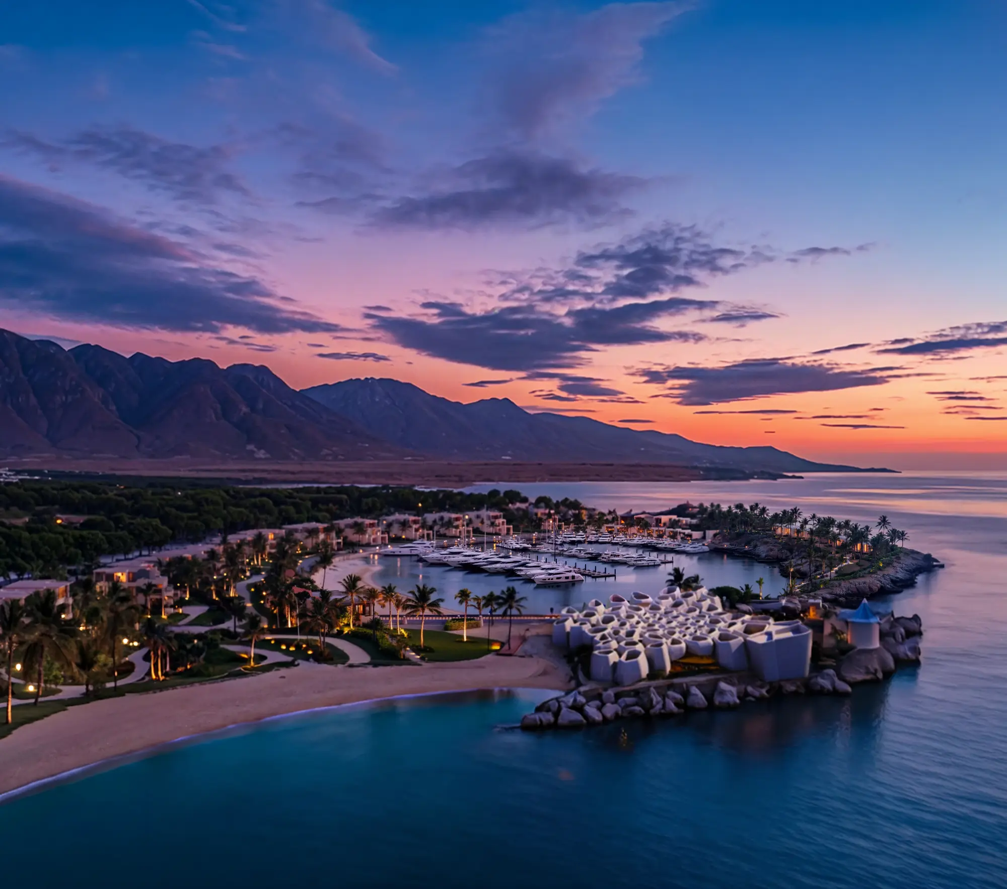 Aerial sunset view of luxury marina resort surrounded by mountains and coastline