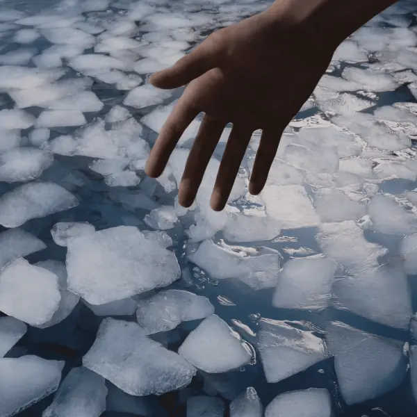 Hand reaching over floating ice in cold water wellness therapy concept