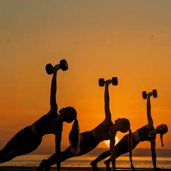 Sunset beach workout session with women performing dumbbell side planks