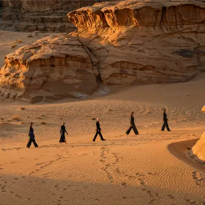 Luxury fashion silhouettes walking across desert dunes beneath sandstone cliffs at golden hour