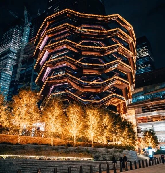 The Vessel lit up at night with festive lights and golden trees in Hudson Yards, NYC