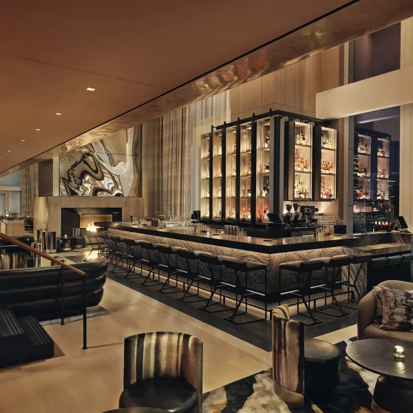U-shaped bar with high chairs, illuminated liquor shelves, fireplace and city view in elegant lounge