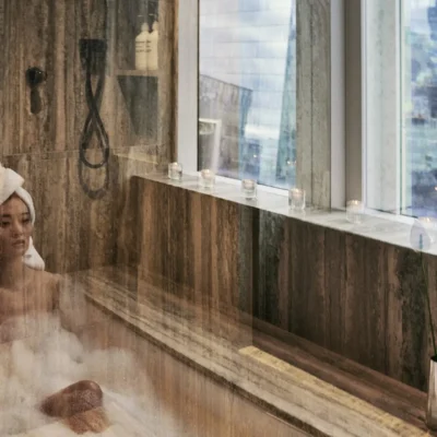 woman in bathtub with view of city skyline seen through bathroom windows at Equinox New York Hotel.
