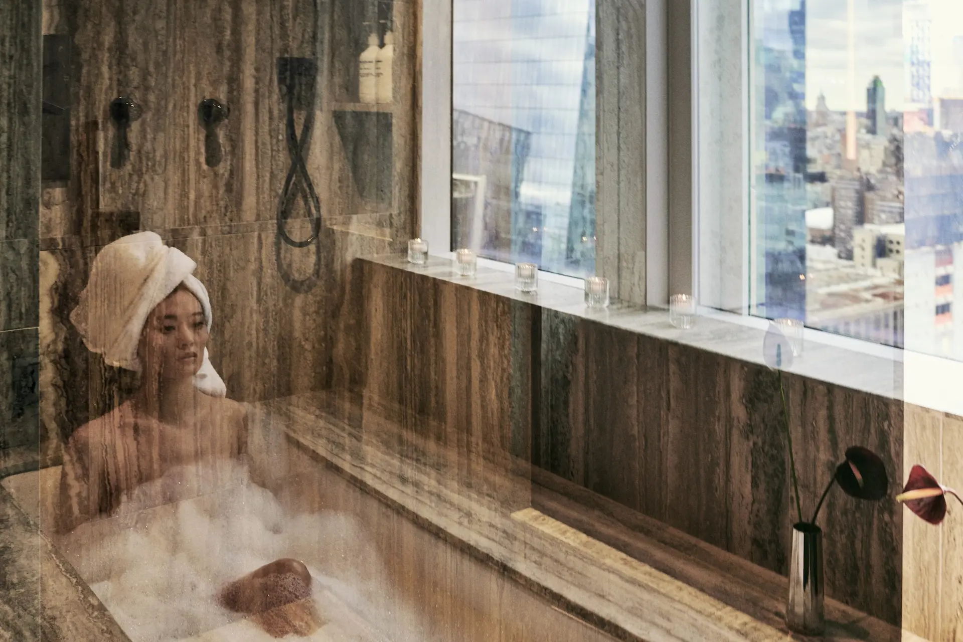woman in bathtub with view of city skyline seen through bathroom windows at Equinox New York Hotel.