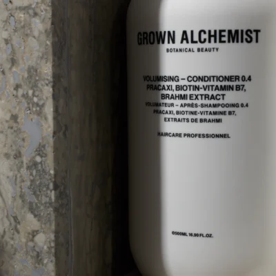 White bottle of Grown Alchemist volumising conditioner placed against textured stone, featuring bilingual label and botanical ingredients