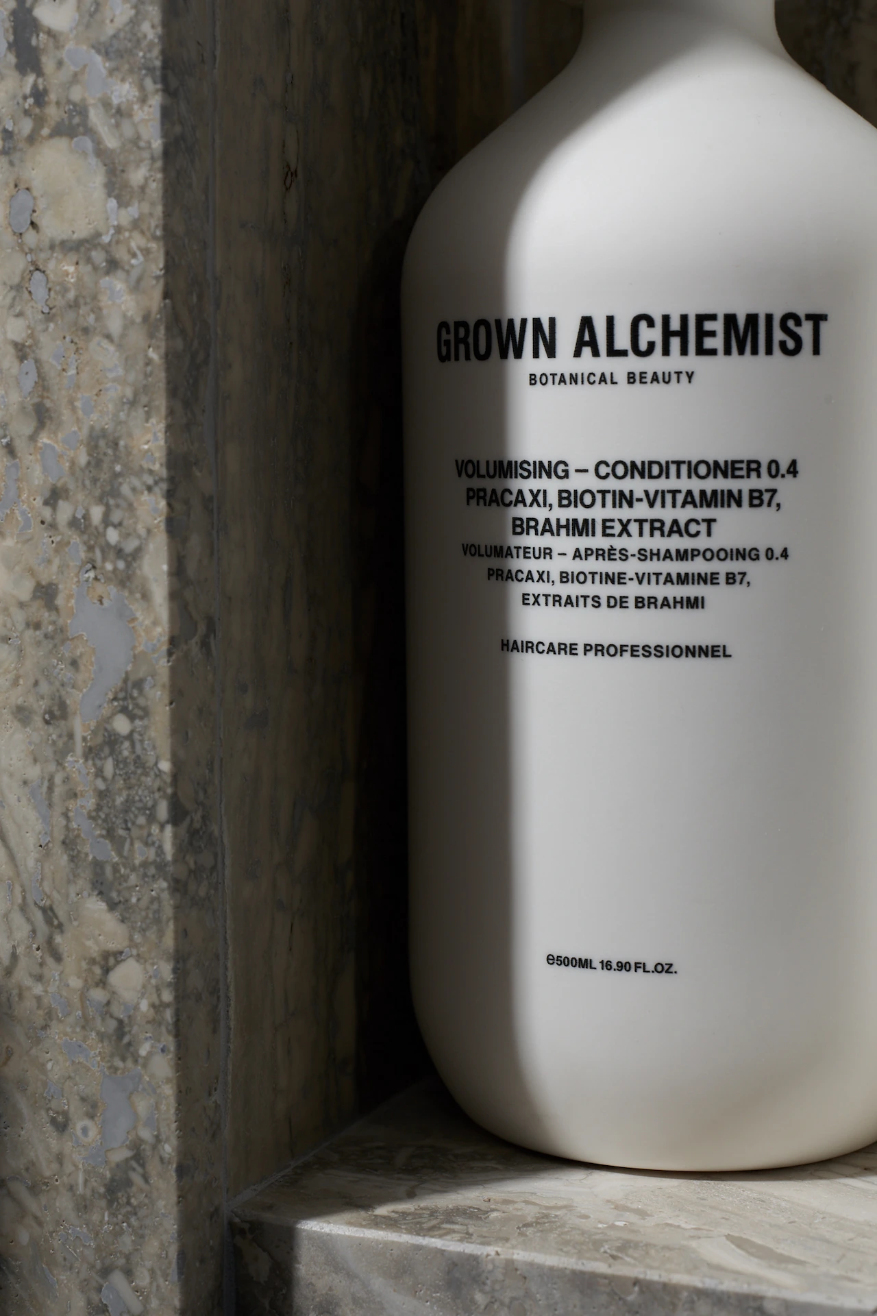 White bottle of Grown Alchemist volumising conditioner placed against textured stone, featuring bilingual label and botanical ingredients