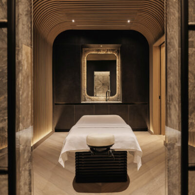 Luxurious spa room with curved wood accents, marble walls, and gold-framed mirror above a massage table.