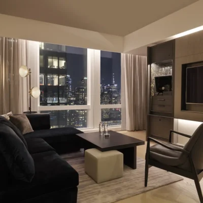Modern living room at night with dark sectional sofa, city skyline through large windows, and built-in cabinetry.