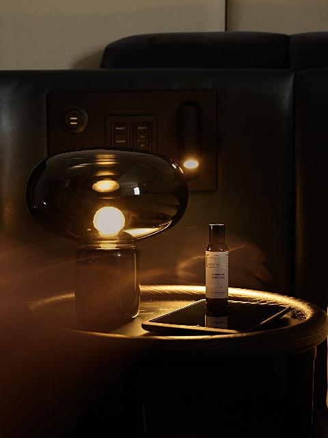 Dimly lit lounge setting with translucent lamp, L'Occitane bottle, and premium seat controls suggesting luxury ambiance.