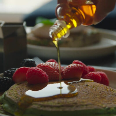 Syrup pours over green pancakes topped with berries, capturing a vibrant and delicious breakfast moment.