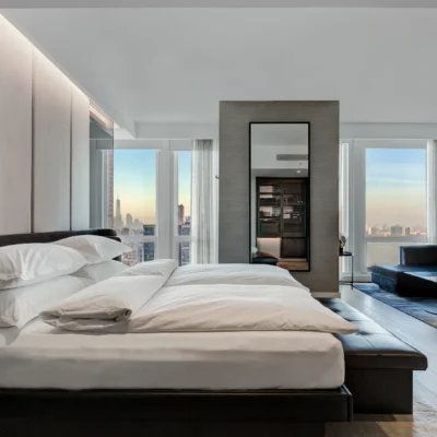 Luxurious hotel bedroom at Equinox New York with sweeping city skyline view at sunset, crisp white linens, sleek modern furnishings, and warm natural light, evoking serene comfort and refined metropolitan elegance.