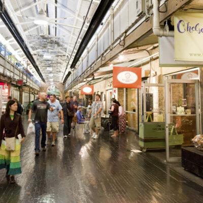Market interior with dark wood floors, exposed pipes, and shops lining a busy corridor.