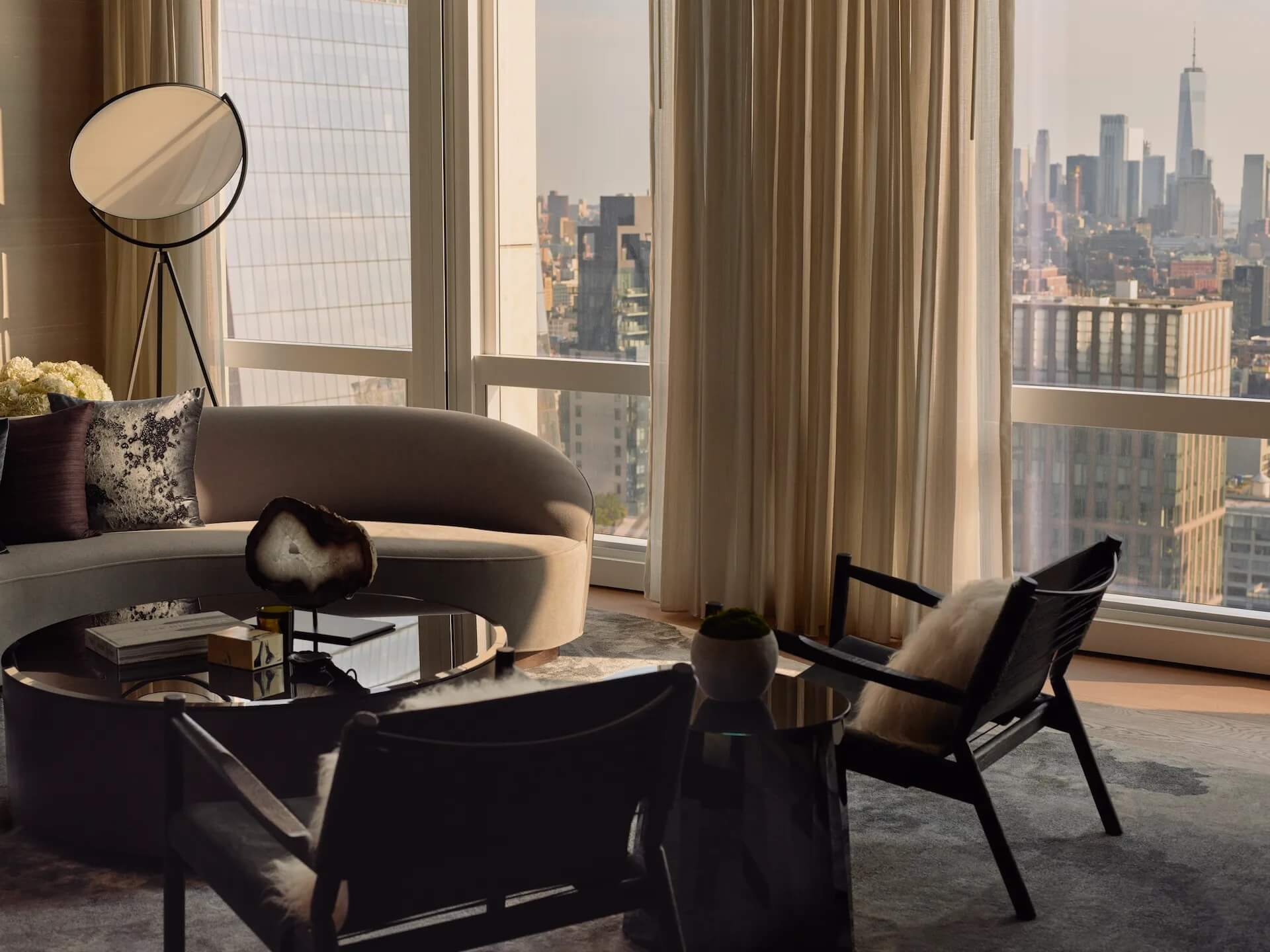 Elegant living room with curved beige sofa, black coffee table, and panoramic city view featuring One World Trade Center.