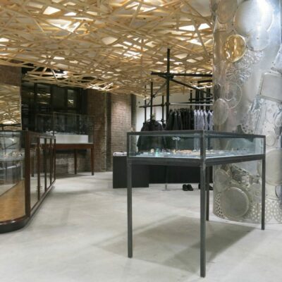 Modern clothing store with wooden slat ceiling, glass displays, and eclectic dishware column.