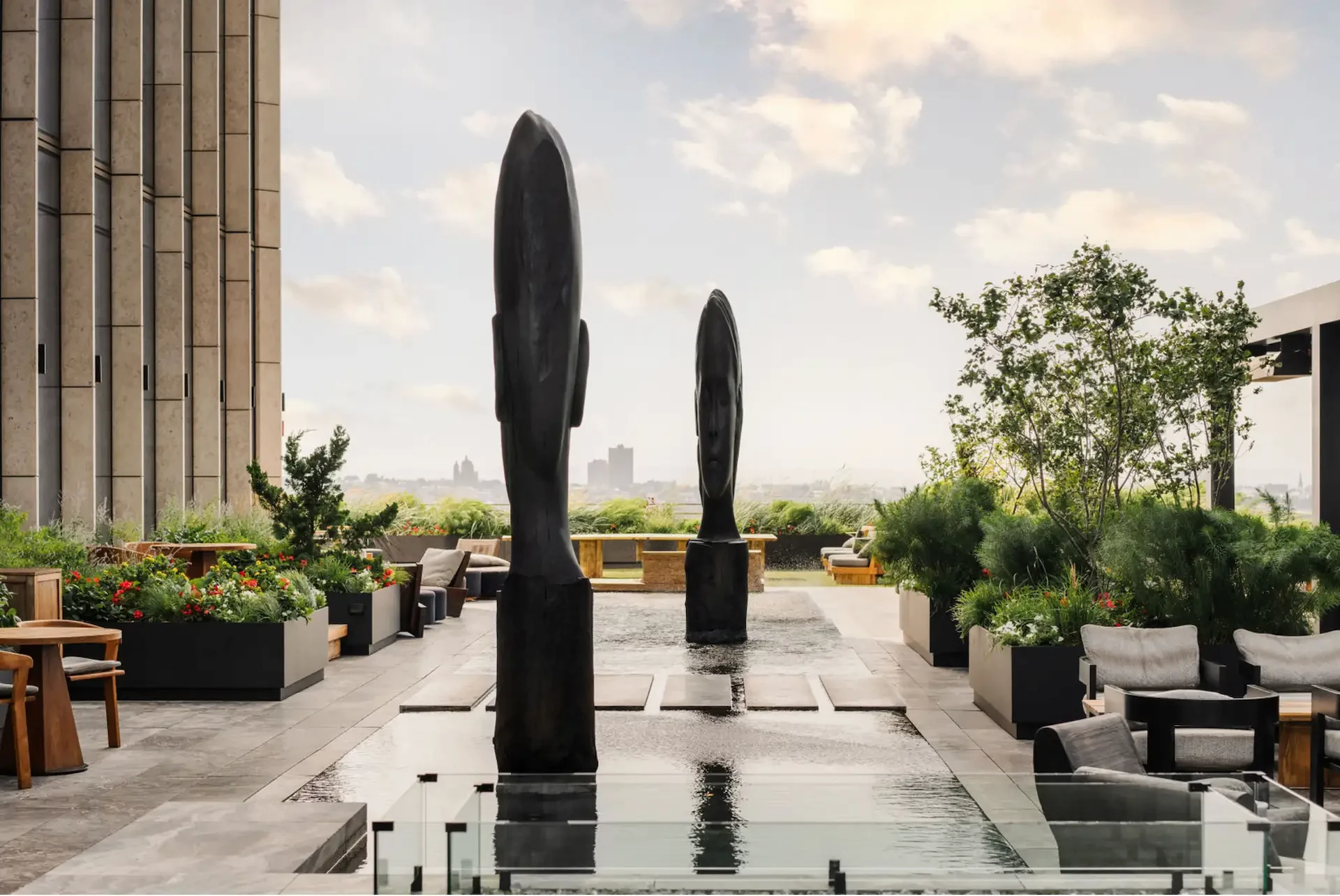 Equinox rooftop terrace with twin head sculptures in reflecting pool, lounge seating, greenery, and city view