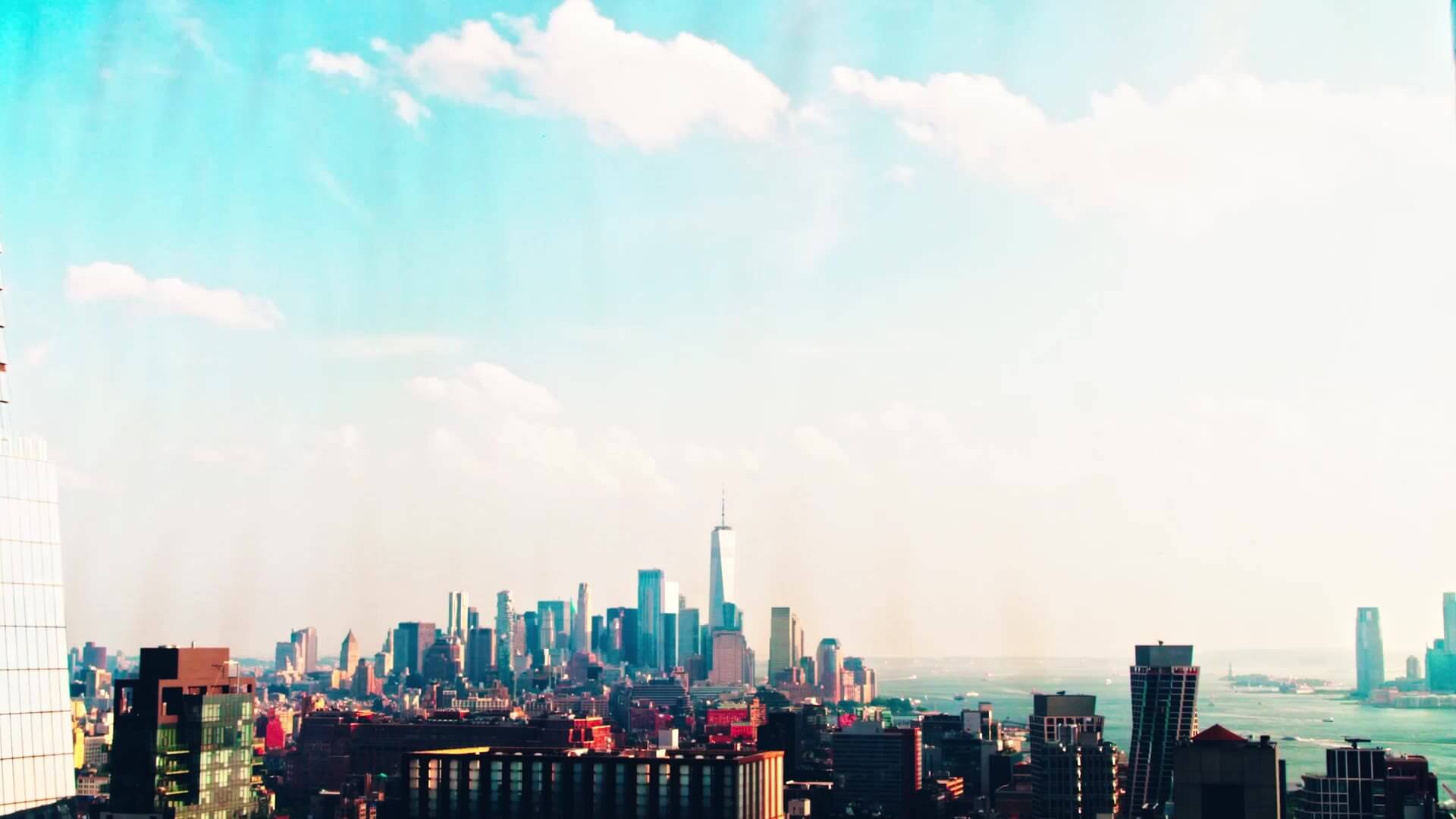 Panoramic view of NYC skyline with One World Trade Center under a partly cloudy sky.