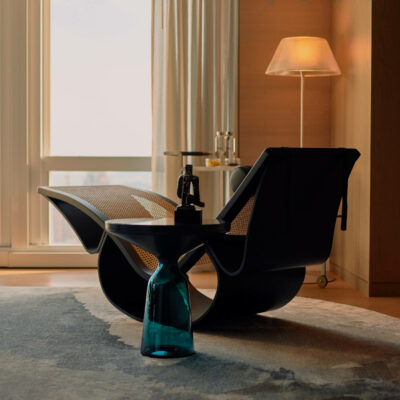 Stylish lounge chair with curved frame, rattan panels, and city view through sheer curtains.