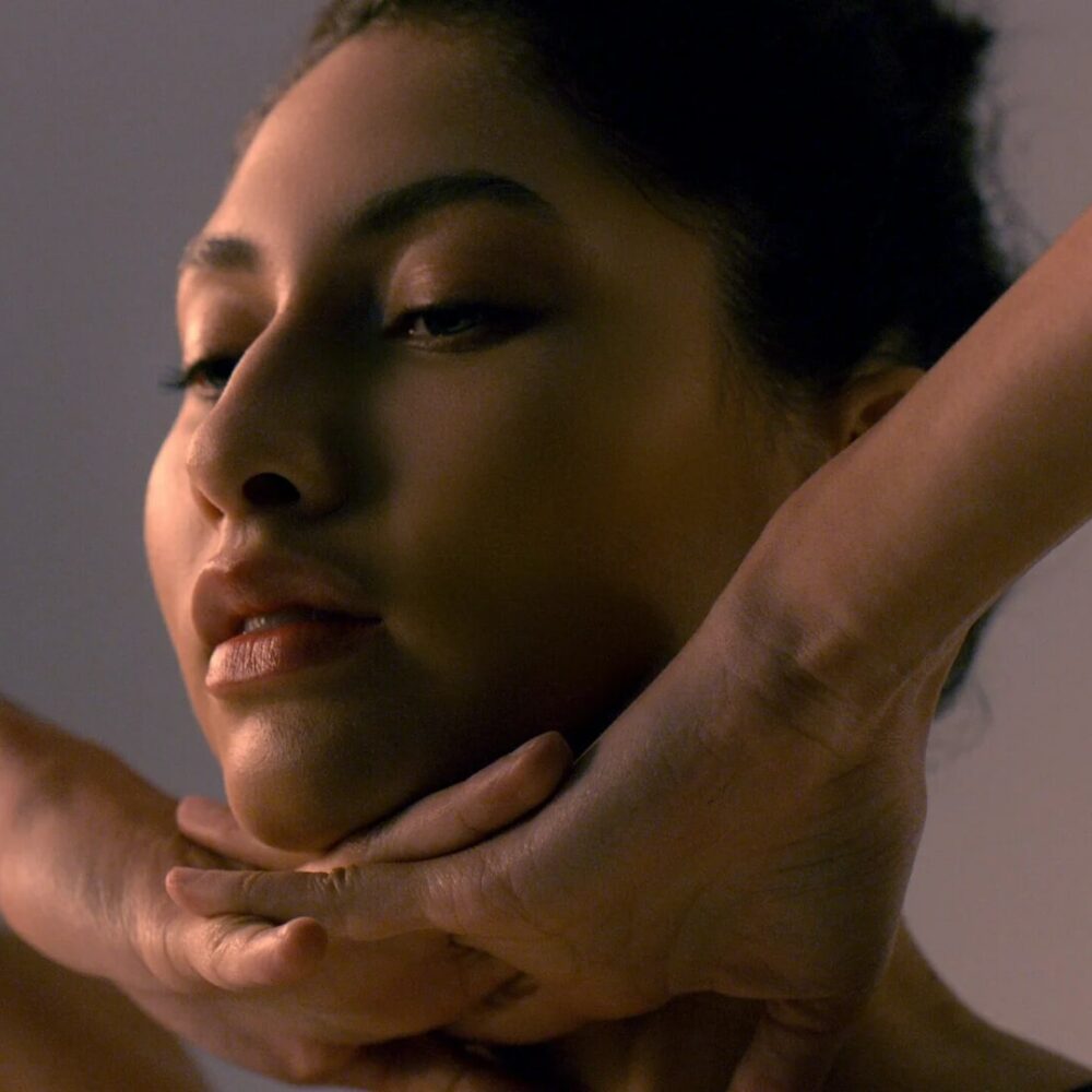 Woman performing facial massage on herself in a serene setting with soft lighting and a calm atmosphere