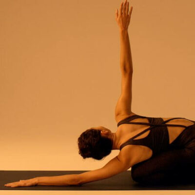 Woman practicing yoga on a mat under warm, ambient lighting; soft shadows and golden tones highlight posture and atmosphere