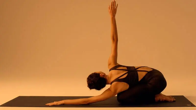 Woman practicing yoga on a mat under warm, ambient lighting; soft shadows and golden tones highlight posture and atmosphere