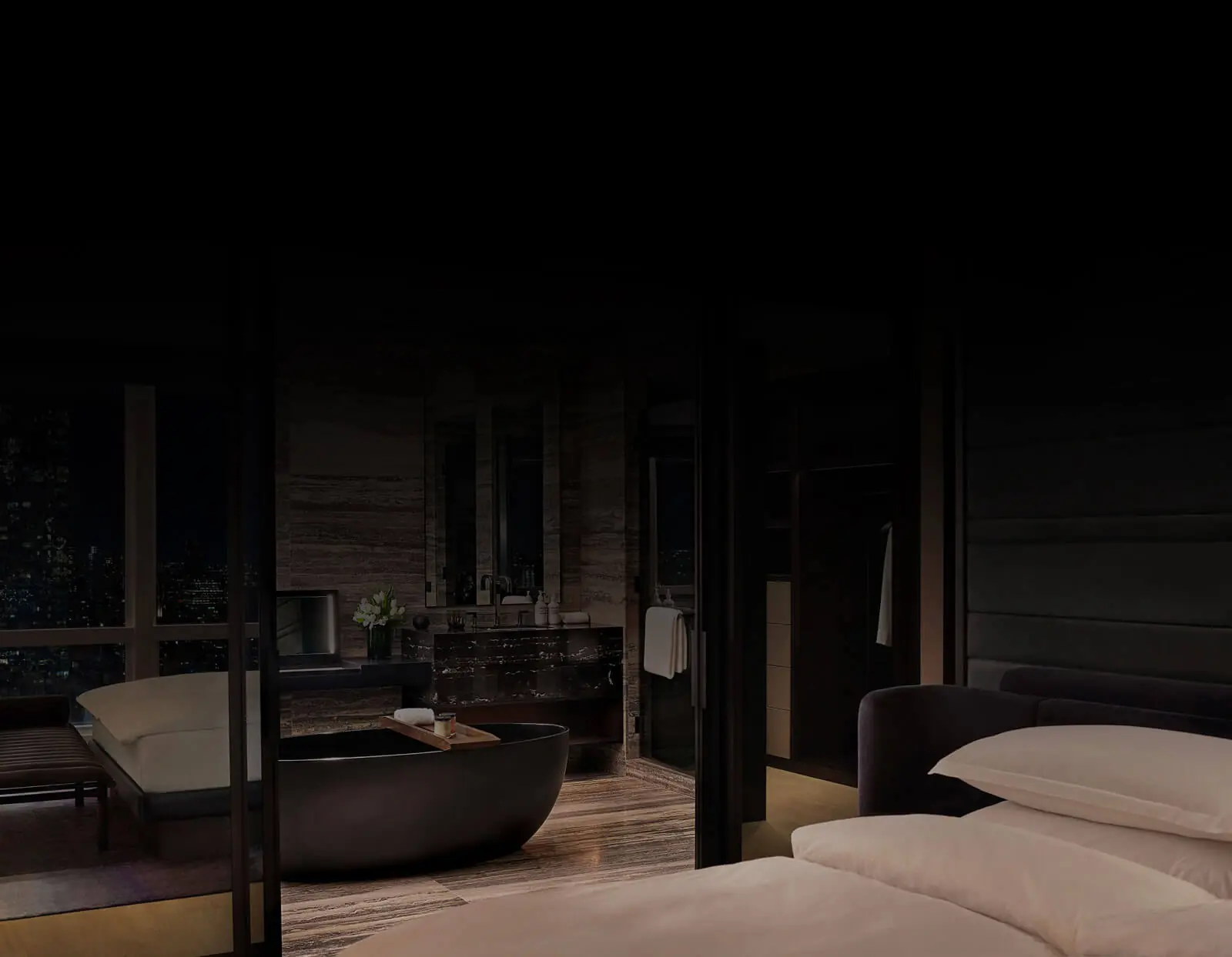 Luxurious suite with white bed, black tub, marble bathroom, and city view through glass partition.