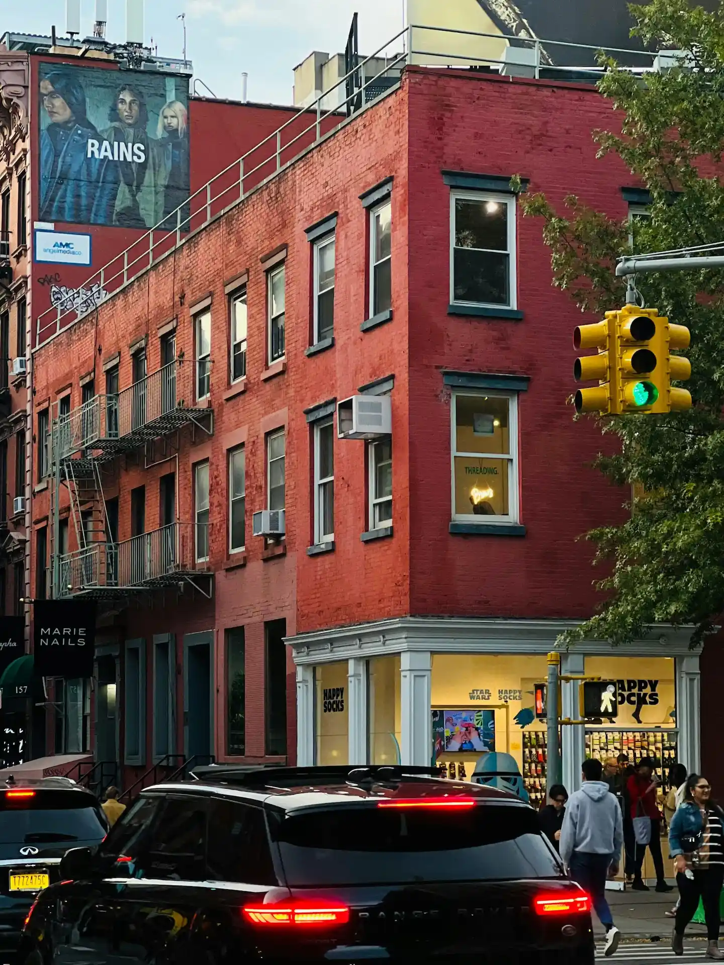 Urban street corner with red brick building, Happy Socks storefront, and pedestrians under AMC billboard
