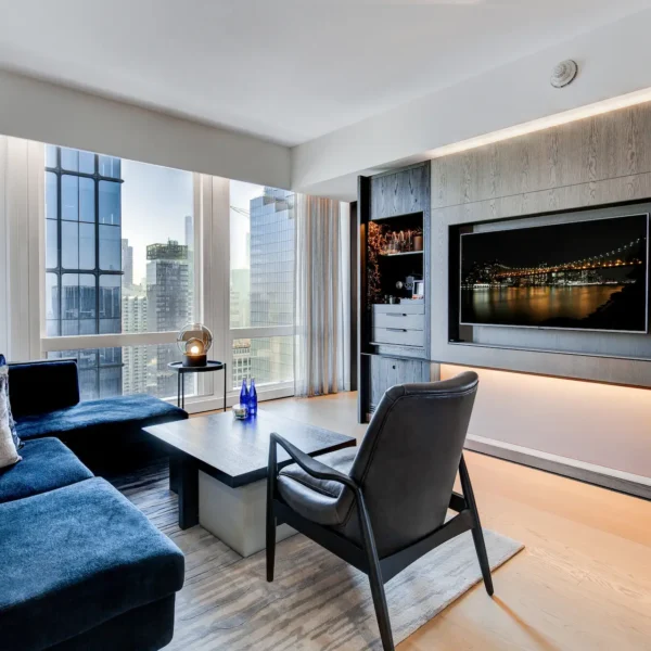Contemporary living room with blue sectional, city views, and illuminated media wall, evoking nighttime elegance and urban comfort