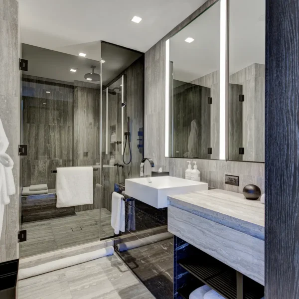 Elegant bathroom with glass shower, dual robes, and stone vanity, evoking spa-like calm and modern refinement