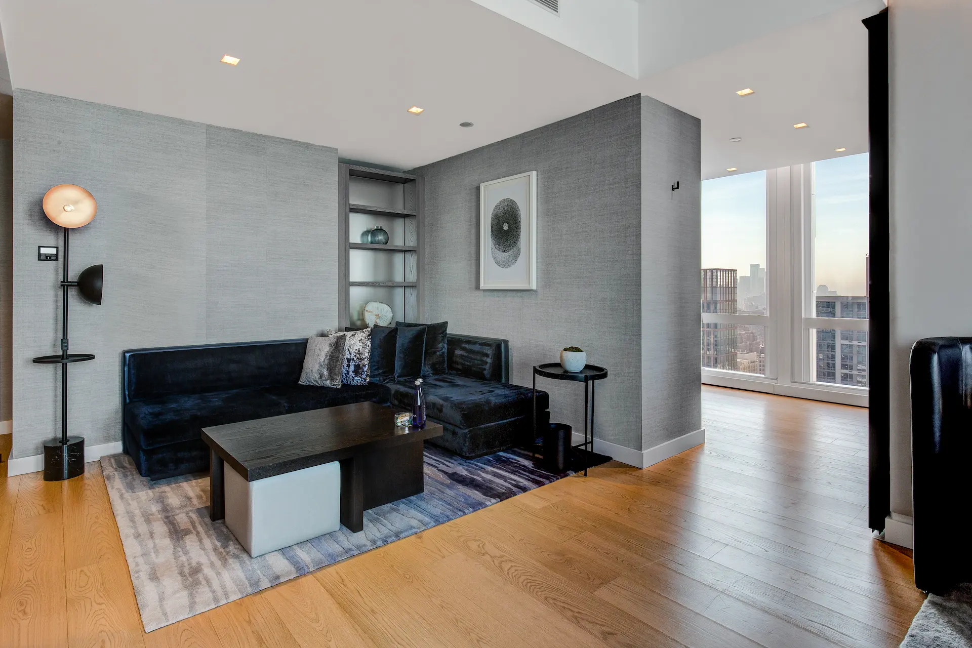 Modern living room with dark sectional sofa, abstract art, and city views, evoking quiet sophistication and urban comfort