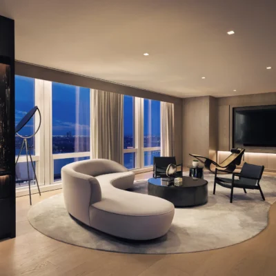 Elegant living room with curved sectional, sculptural lounge, and dusk city views, evoking refined comfort and artistic urban living