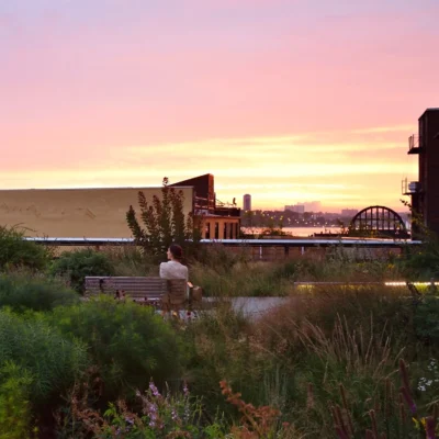 woman sitting on bench on the highline viewiing sunset over hudson river