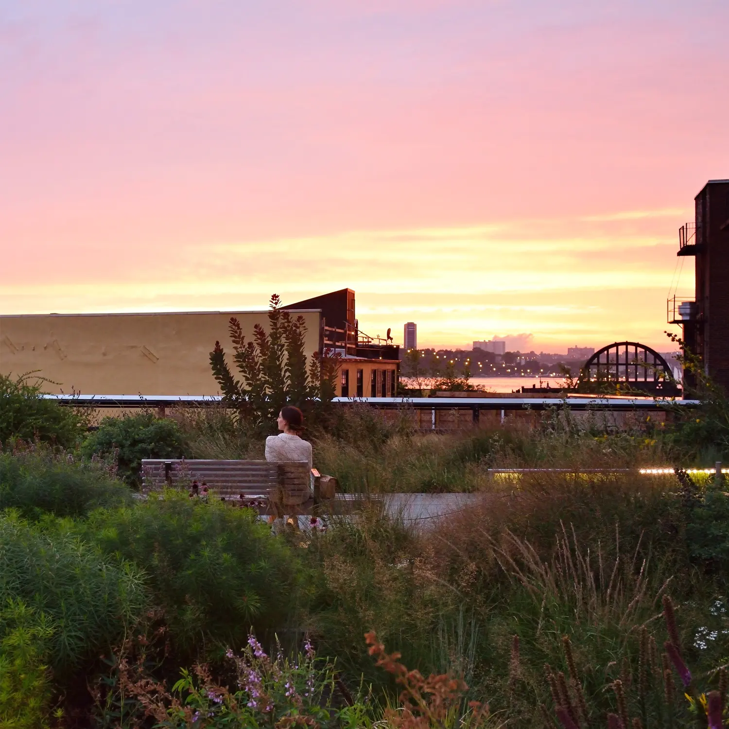 woman sitting on bench on the highline viewiing sunset over hudson river