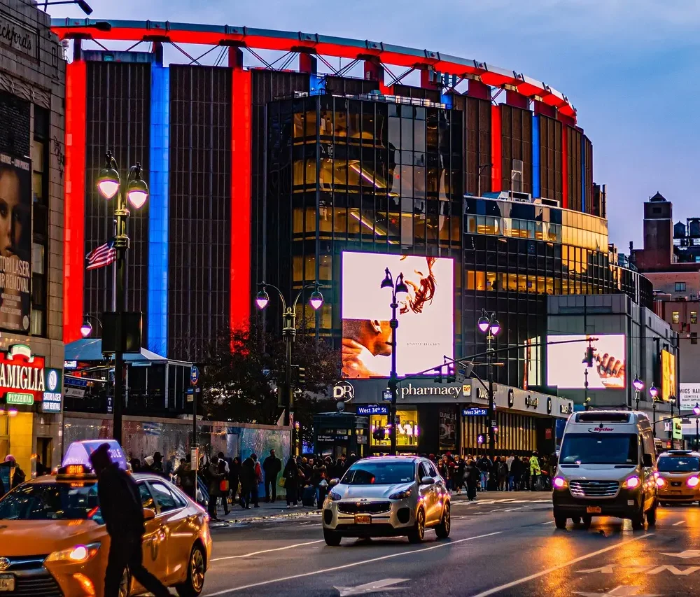 Evening street scene outside Madison Square Garden with neon lights, taxis, and bustling pedestrians