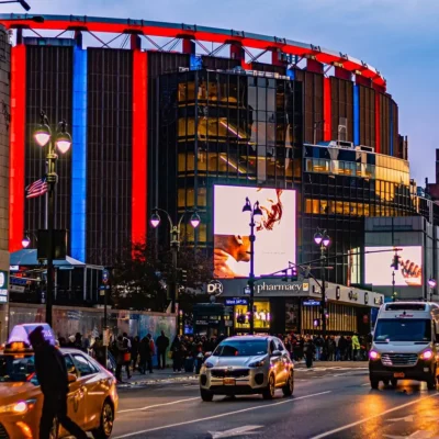 Evening street scene outside Madison Square Garden with neon lights, taxis, and bustling pedestrians