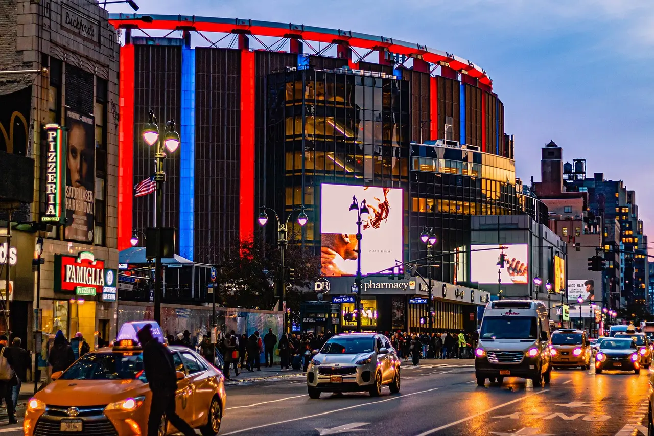 Evening street scene outside Madison Square Garden with neon lights, taxis, and bustling pedestrians