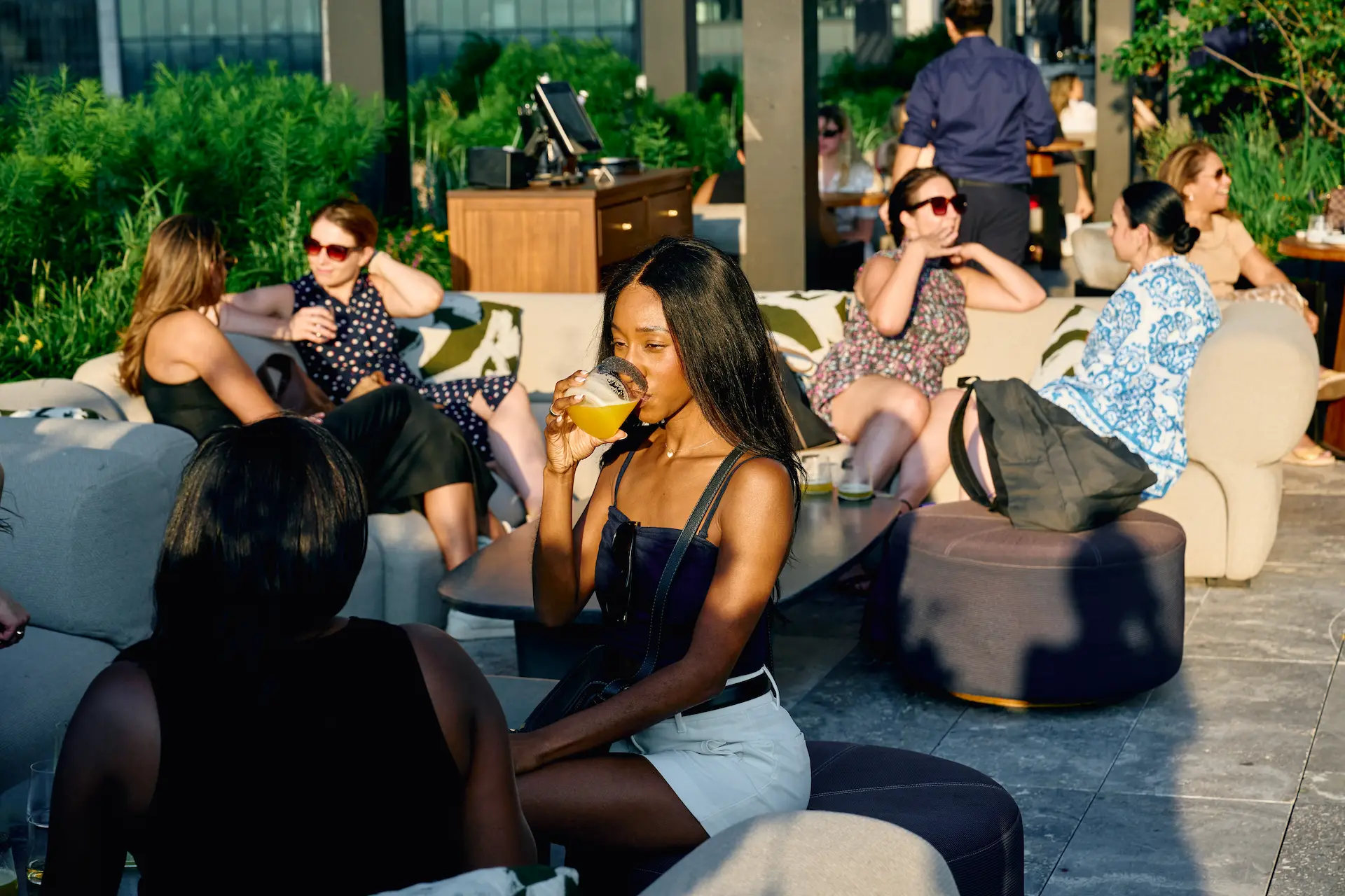 People enjoying drinks at outdoor lounge with plants and city views, evoking relaxed social vibe