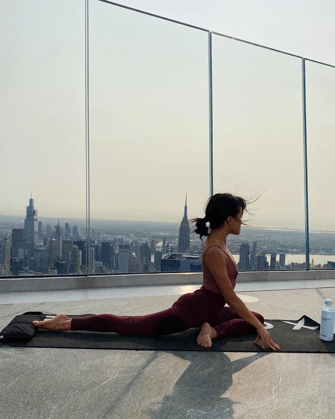 Woman practicing pigeon yoga pose on the edge of an observation deck at Equinox Hotel New York, with sweeping views of the Empire State Building and iconic NYC skyline at golden hour, blending mindfulness, motion, and urban energy.
