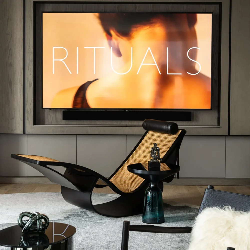 Modern lounge with sculptural black chairs, rattan accents, sleek TV displaying 'RITUALS', and warm wood-paneled walls