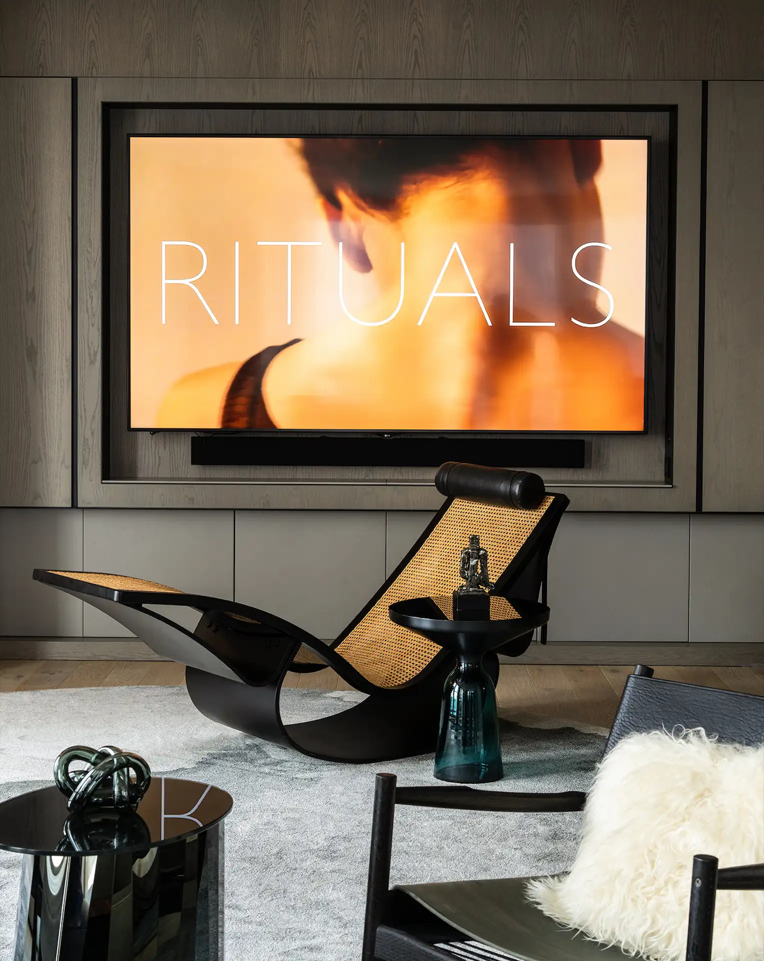 Modern lounge with sculptural black chairs, rattan accents, sleek TV displaying 'RITUALS', and warm wood-paneled walls
