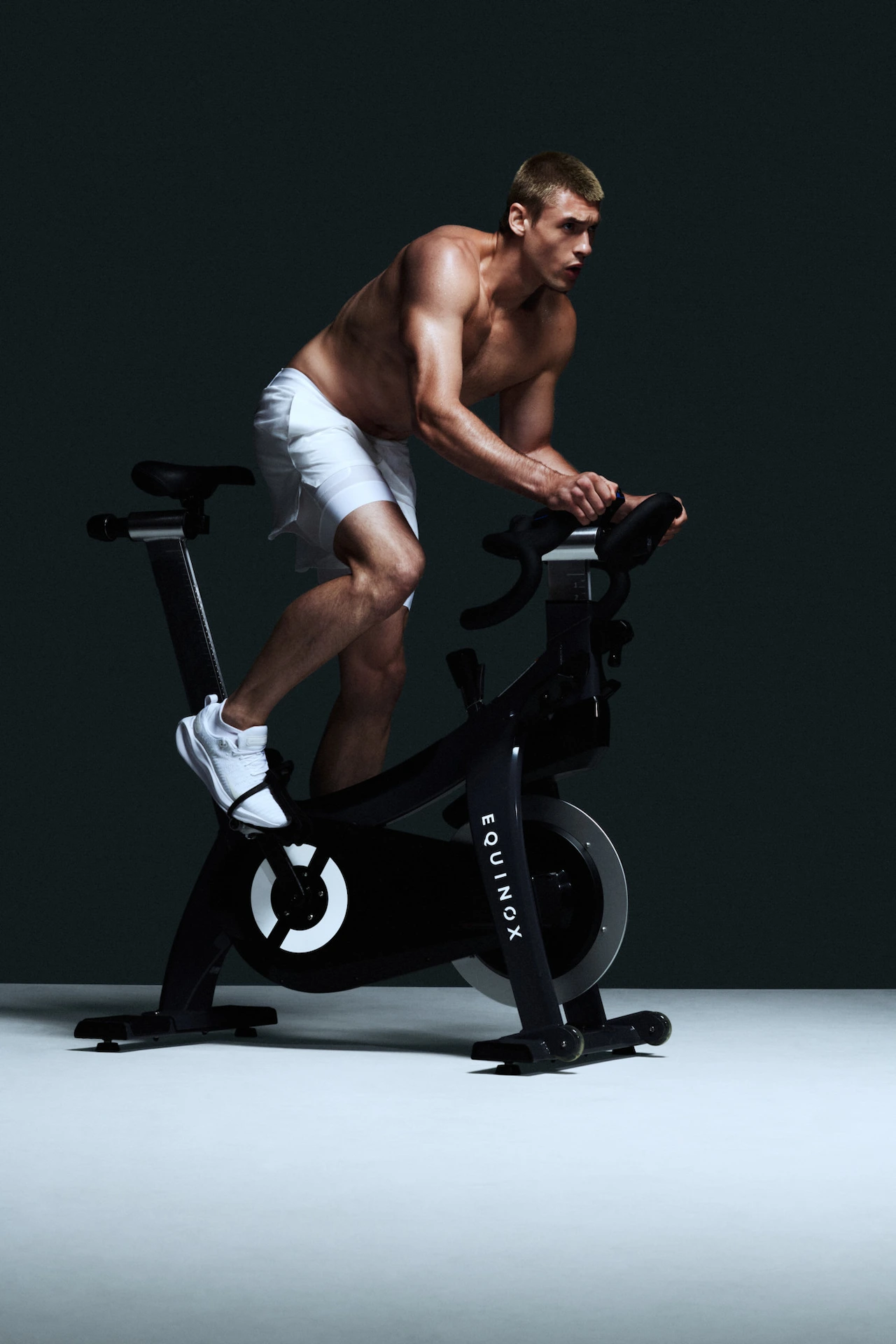 Individual riding Equinox-branded stationary bike in dark setting, evoking intensity, focus, and elevated cardio training