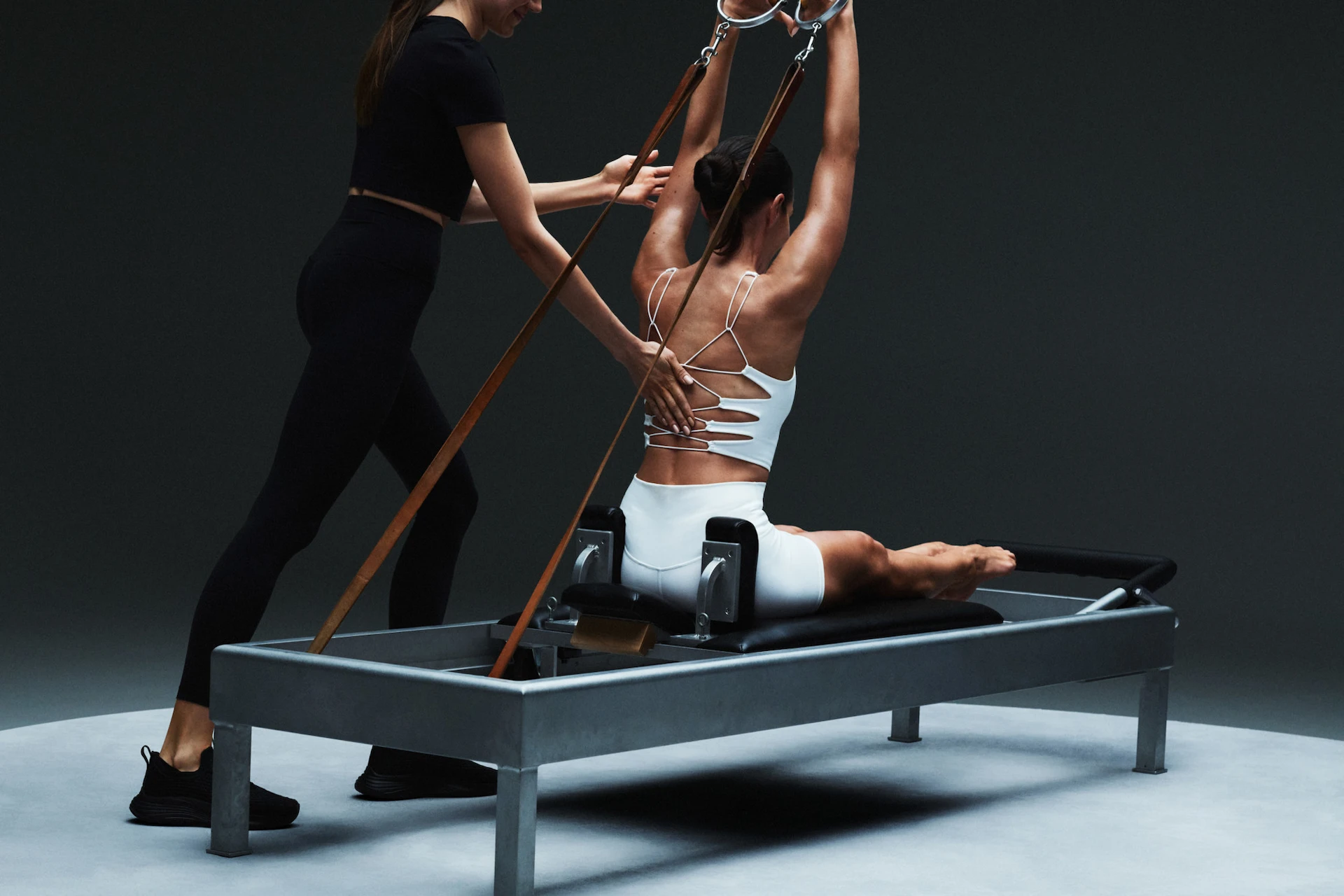 Individual performing Pilates on reformer machine with instructor guidance, set in minimalist studio, evoking precision, alignment, and elevated training
