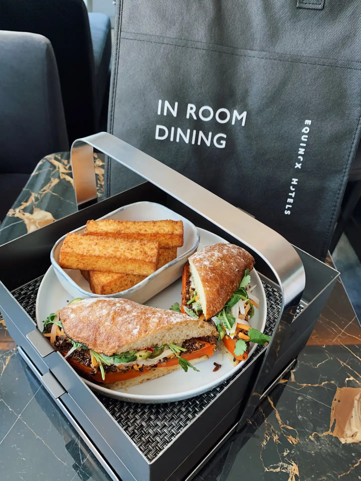 Tray with sandwich halves and toasted bread sticks, on marble table with Equinox Hotels bag.