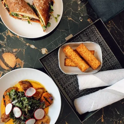 Top-down view of gourmet meal on dark marble table with sandwich, meat dish, fried items, and napkin set.