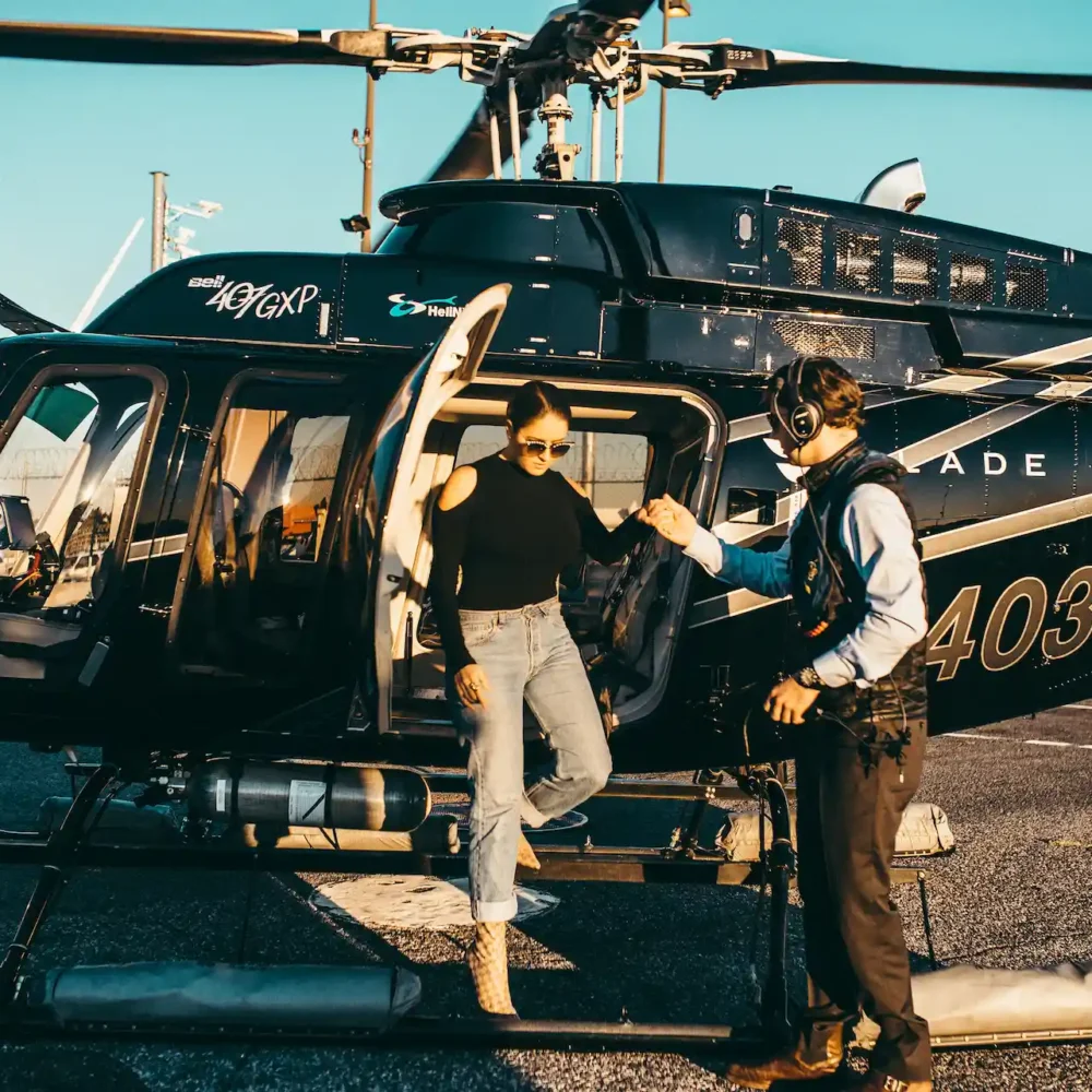 Person stepping out of black helicopter on tarmac with crew member assisting, suggesting luxury or organized air transport