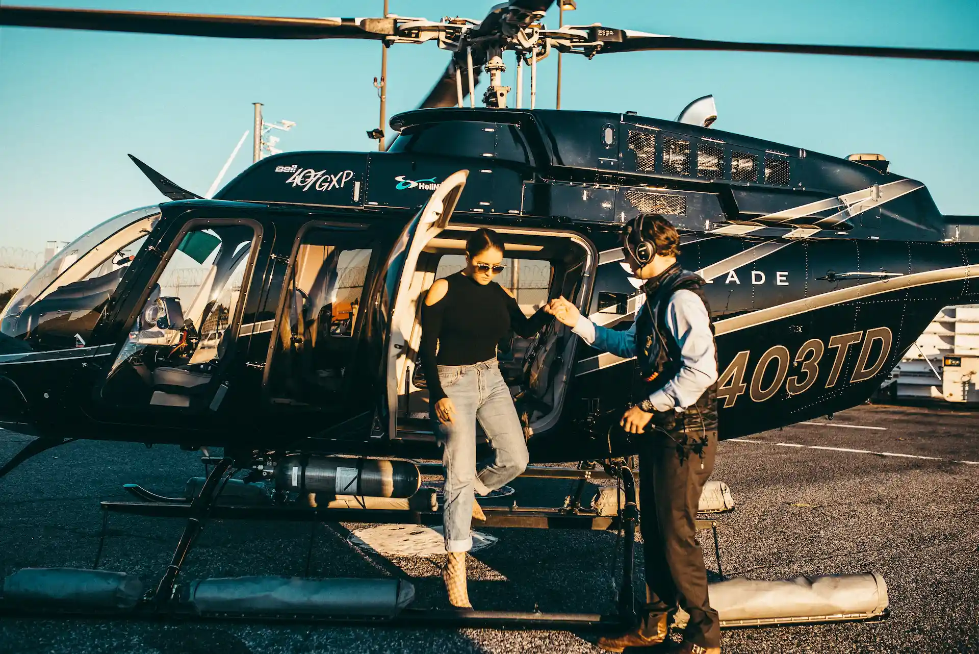 Person stepping out of black helicopter on tarmac with crew member assisting, suggesting luxury or organized air transport