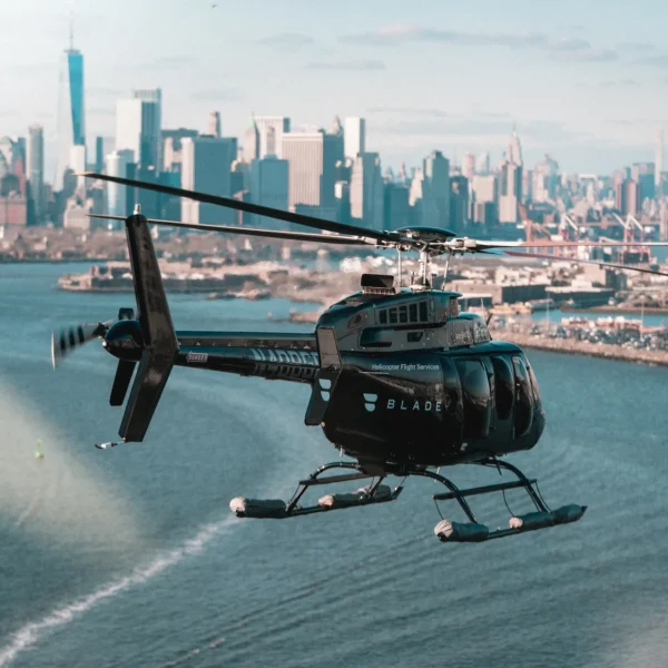 Black BLADE helicopter flying low over water with NYC skyline in background, highlighting luxury urban air travel