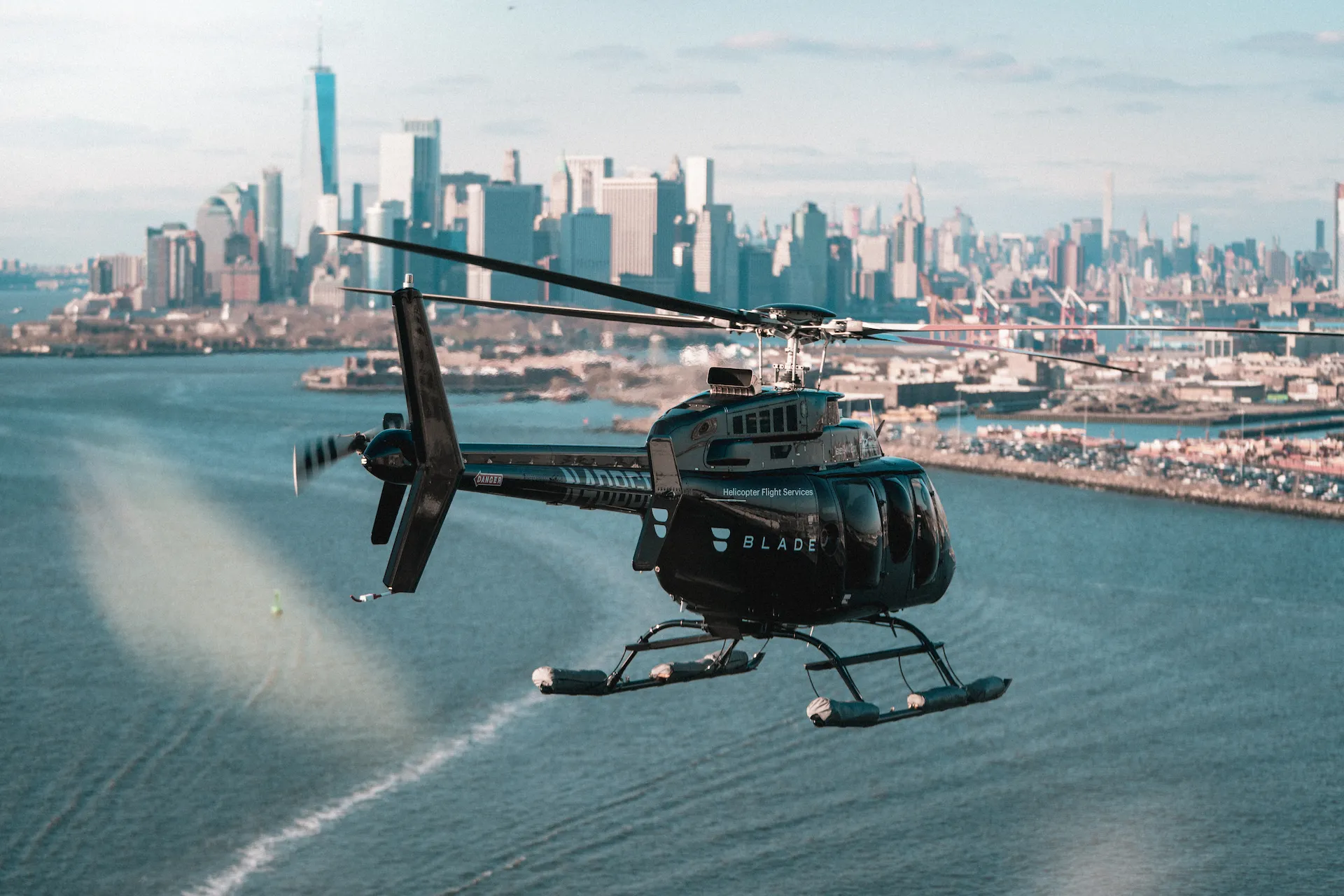 Black BLADE helicopter flying low over water with NYC skyline in background, highlighting luxury urban air travel