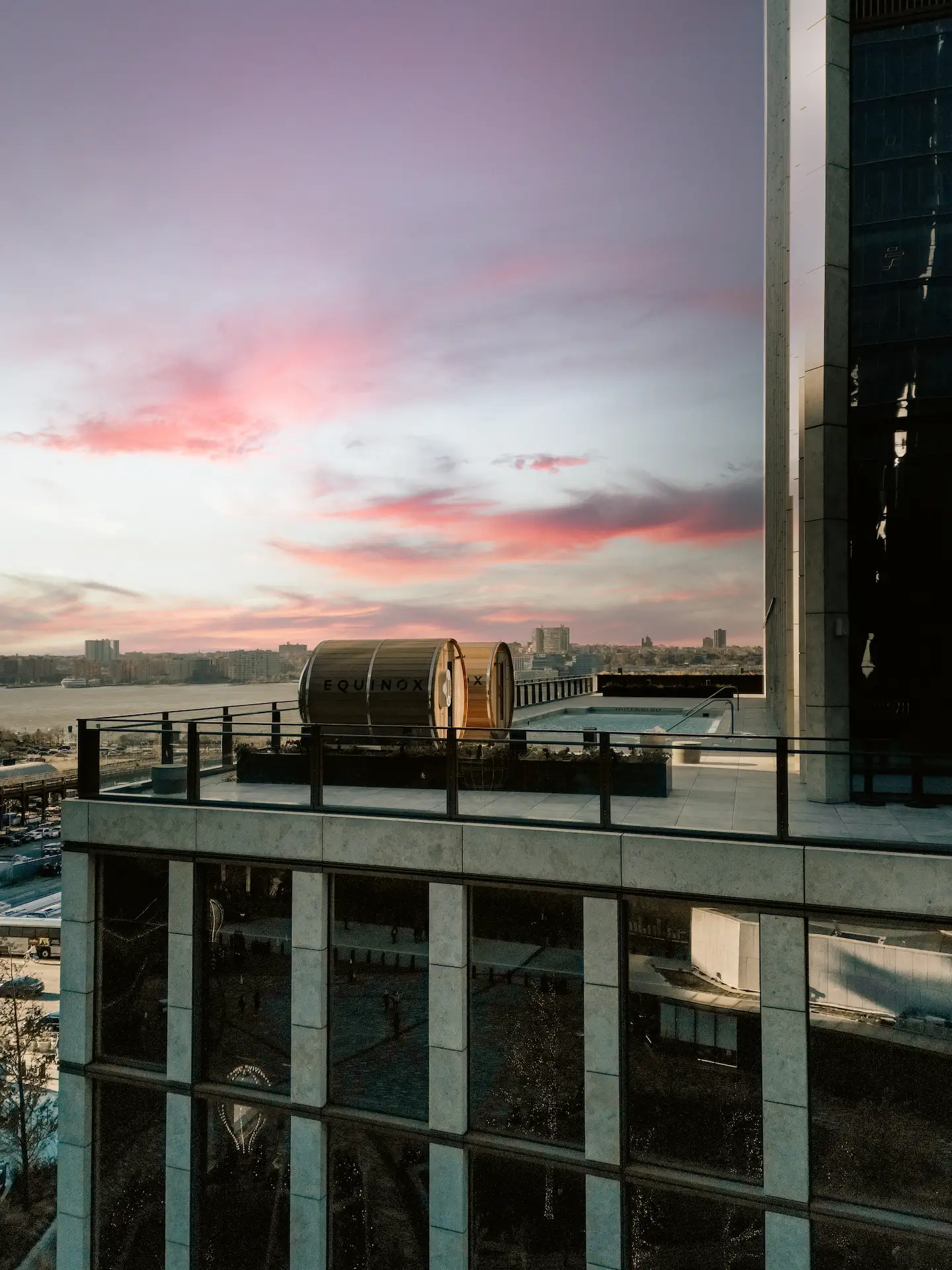 Sunset rooftop view with two “SQUARES” structures, glass railing, and cityscape fading into pink and blue sky over water