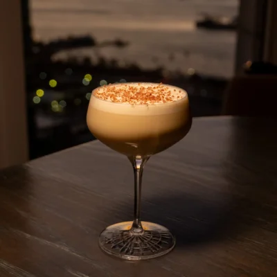 Creamy cocktail on dark table with sunset city view over water, evoking quiet indulgence